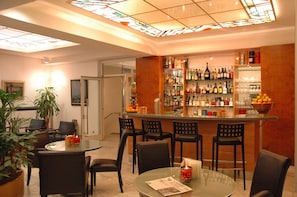 A bar area with a glass top table, bar stools, and a variety of bottles and glasses on shelves. - Hotel Unger (Stuttgart)