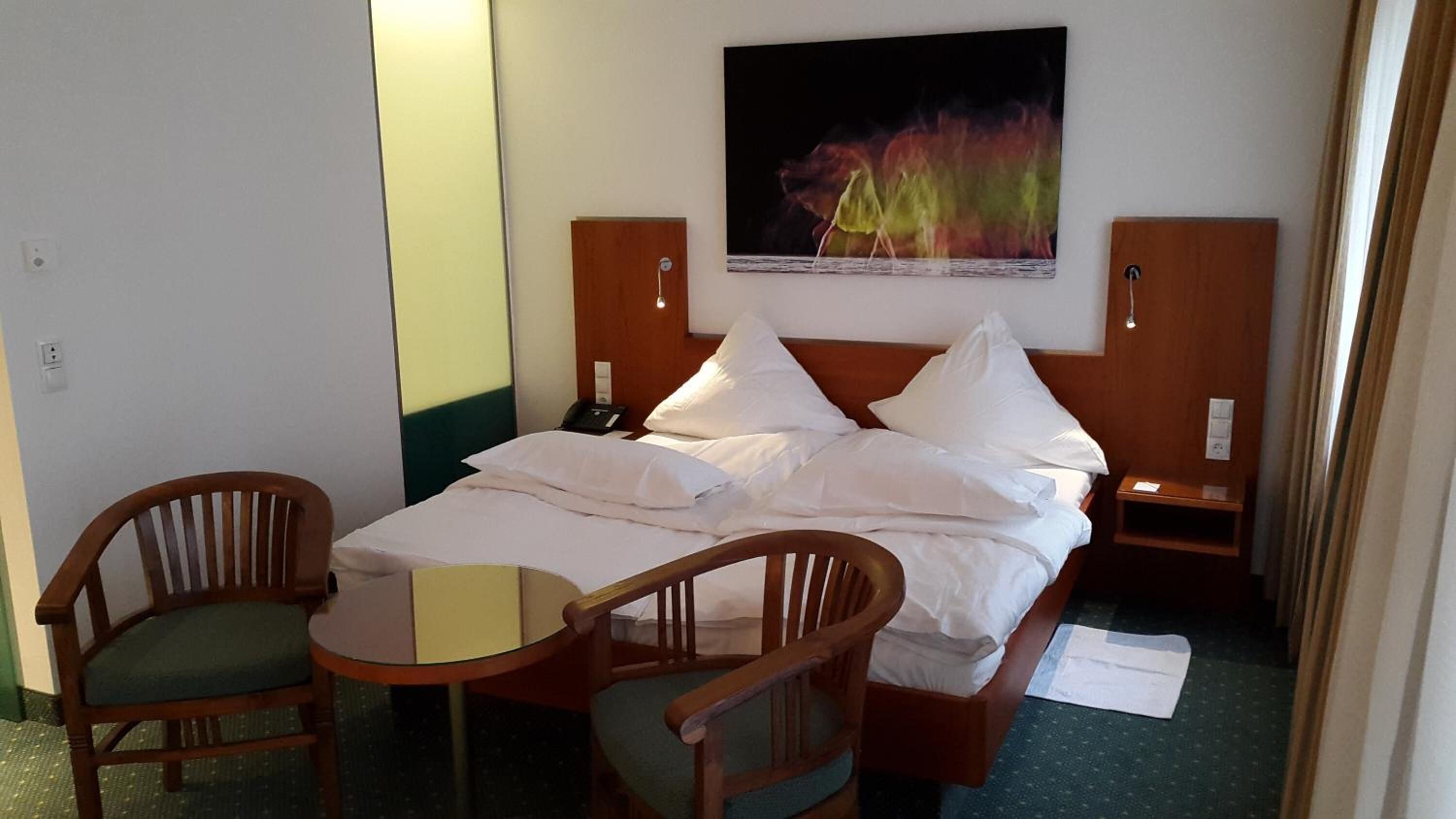 Une chambre d’hôtel avec un lit, deux chaises, une table, un tableau et une table de chevet.