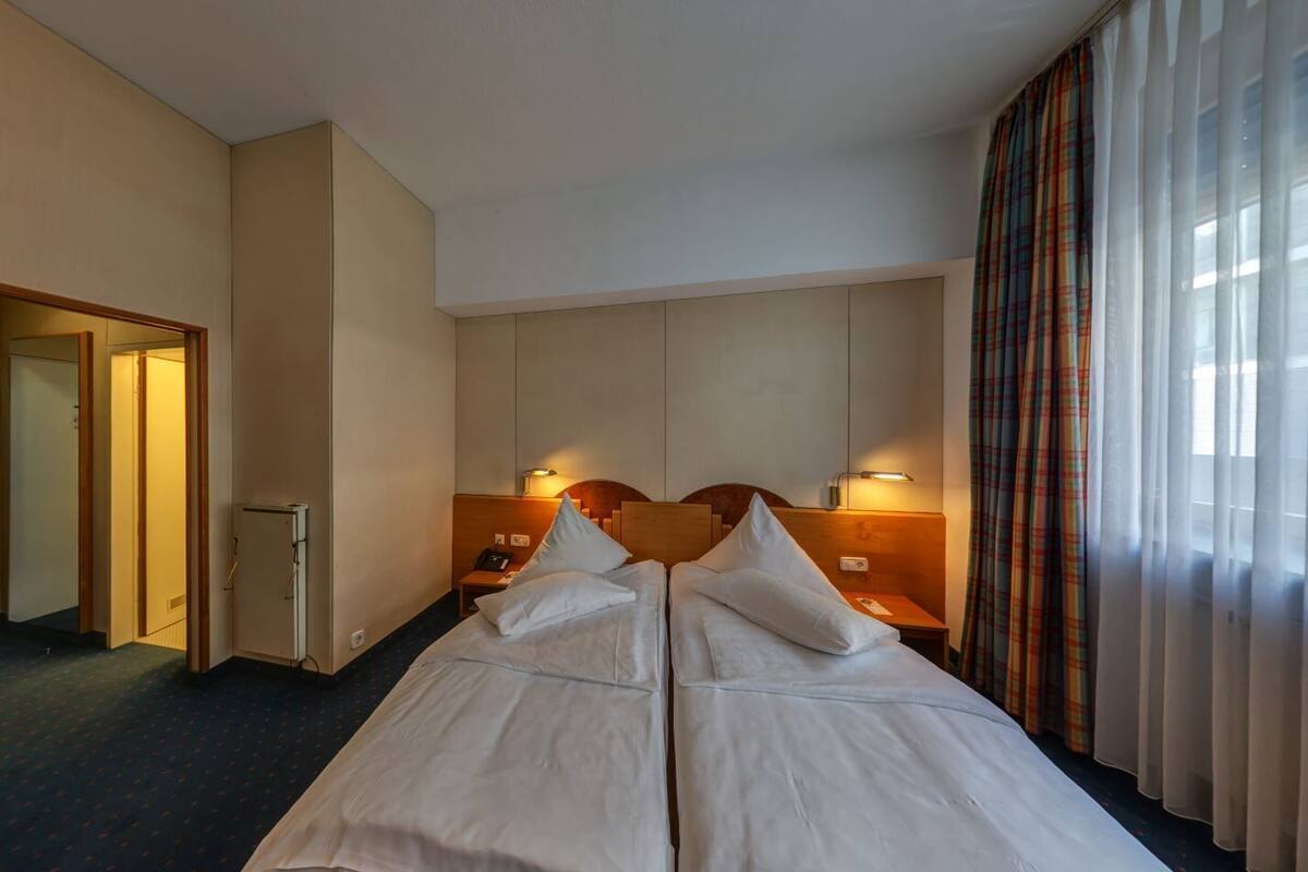 A hotel room with two beds, a small desk, a mirror, and a wardrobe.