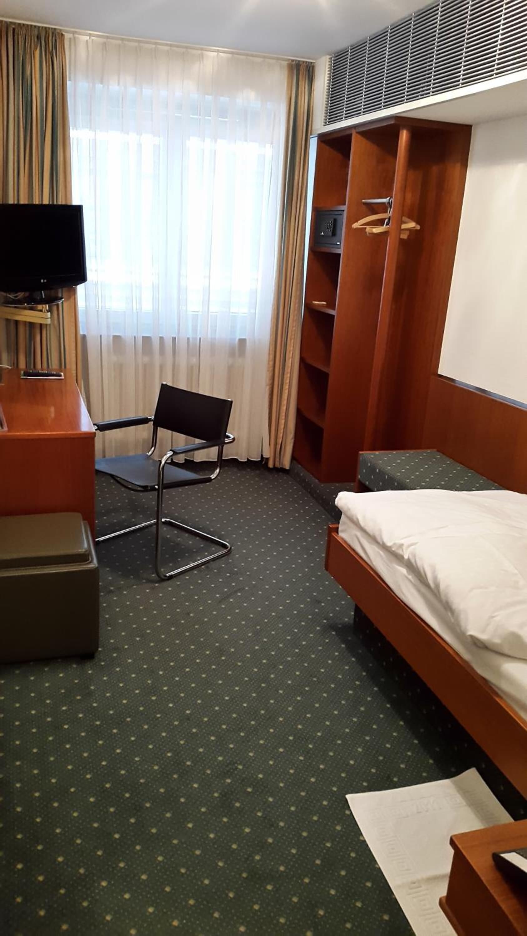 A hotel room with a bed, a chair, a desk, a wardrobe, and a television.