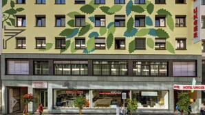 Un edificio de hotel con fachada con motivos de hojas, múltiples ventanas y locales comerciales, incluyendo una cocina y un restaurante.