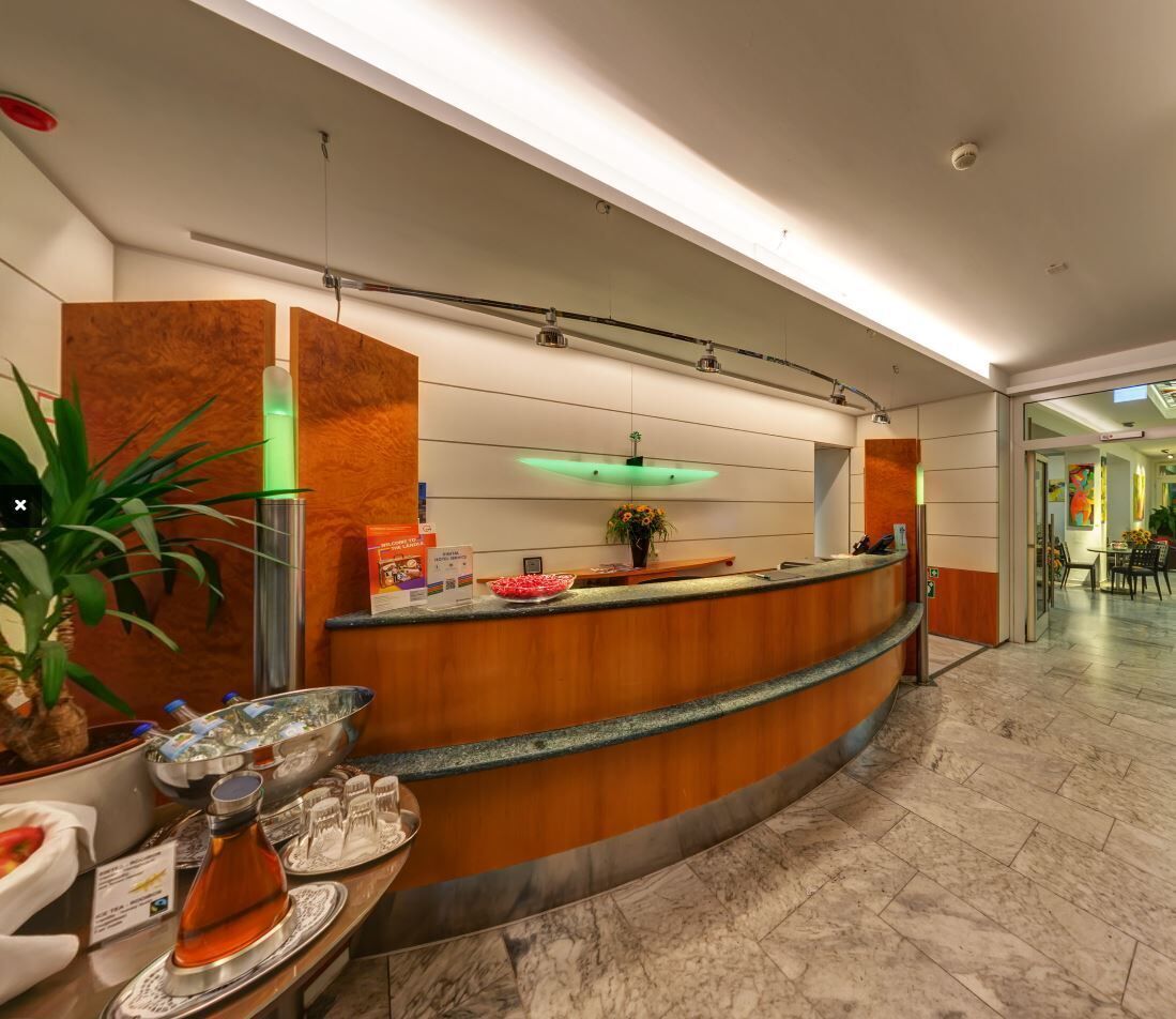 A modern reception area with a curved wooden counter, a green-lit ceiling, and a marble floor.