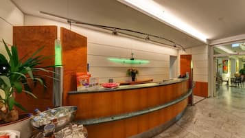 A modern reception area with a curved wooden counter, a green-lit ceiling, and a marble floor.