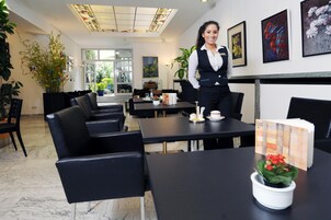 Un moderno vestíbulo de hotel con sillones de cuero negro, una mesa de recepción y una planta en maceta.