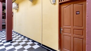 Un pasillo con piso a cuadros, una puerta marrón con el número 102 y unidades de aire acondicionado en la pared.