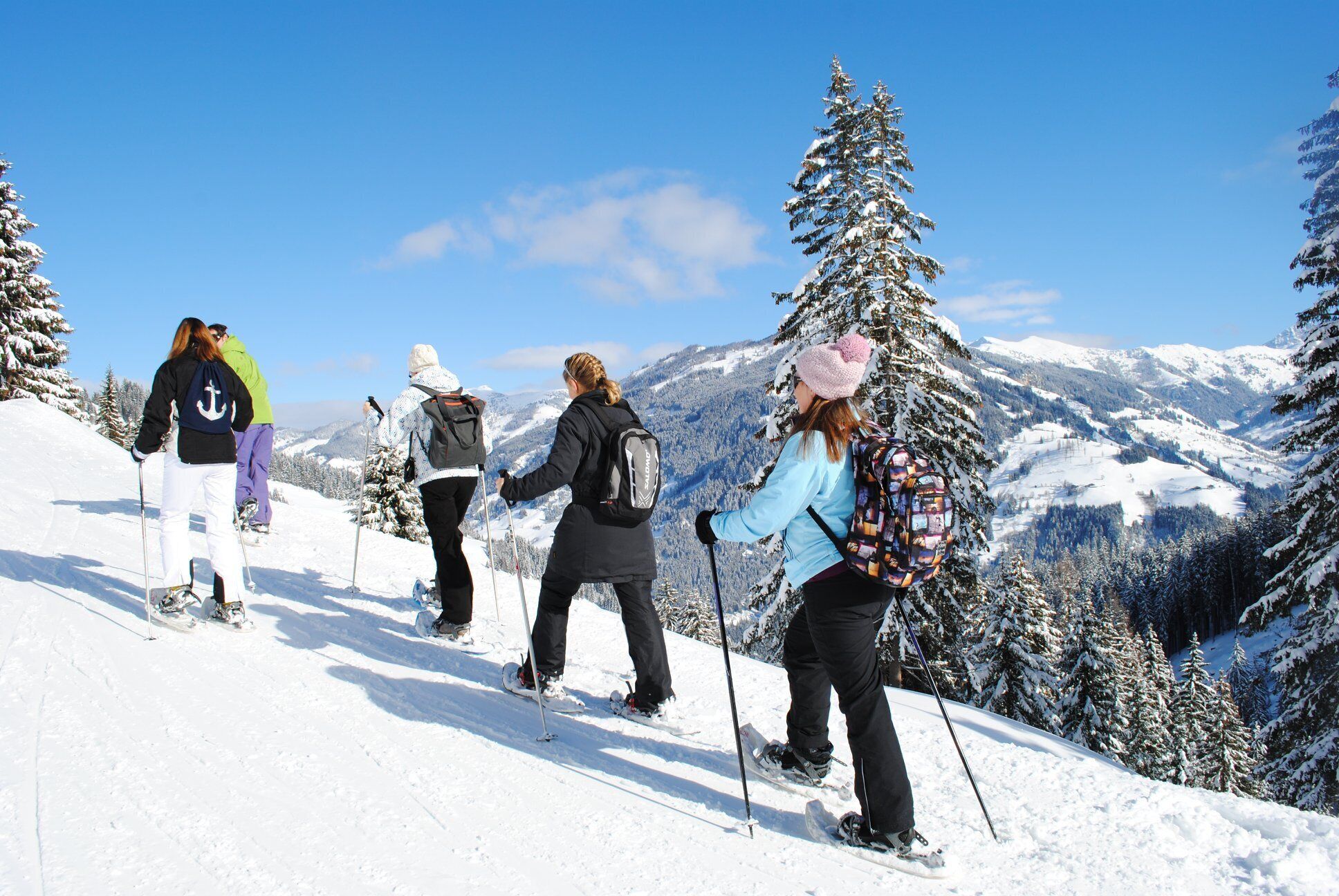 Eine Gruppe Wanderer auf einem verschneiten Bergpfad, im Hintergrund verschneite Bäume und Berge.