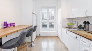 A modern kitchen with white cabinets, a wooden countertop, and a window. There are two bar stools and a dishwasher. - Deluxe 4 BR Oxford Circus Apartment with Terrace (London)