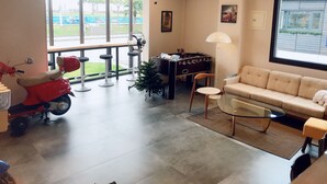 A room with a sofa, a foosball table, a scooter, a Christmas tree, and a window with a view of a pool. - One Way B&B (Hualien City)
