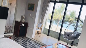 A hotel room with a bed, a glass table, a sofa, a hanging chair, a desk, and a view of the beach. - One Way B&B (Hualien City)