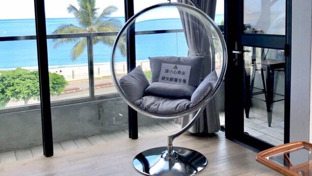 A modern living room with a hanging chair, large windows, and a view of the ocean. - One Way B&B (Hualien City)