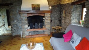 A stone-walled room with a fireplace, a sofa with colorful cushions, and a wooden floor. - Typical Cevennes house for people with mountain view (Mialet)