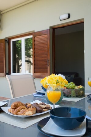 A breakfast table with croissants, cookies, a fruit basket, a glass of orange juice, and a vase of flowers. - Newly renovated Garden Flat (Chania)