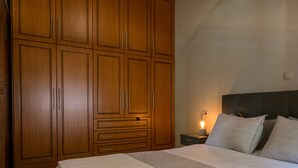 Une chambre avec une grande armoire en bois, un lit avec une literie blanche et une table de chevet avec une lampe.