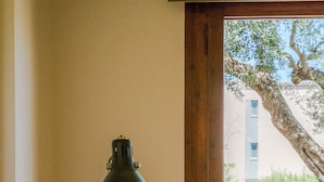Une pièce avec un fauteuil rouge, un lampadaire et une fenêtre donnant sur un immeuble et des arbres.