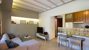 Un salon comprenant un canapé, une table basse, un téléviseur et un petit coin cuisine avec une table à manger et des chaises.