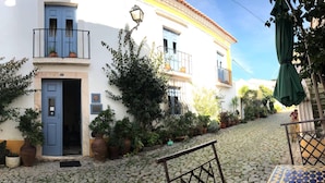 Un edificio con un patio adoquinado, una puerta azul y macetas con plantas.