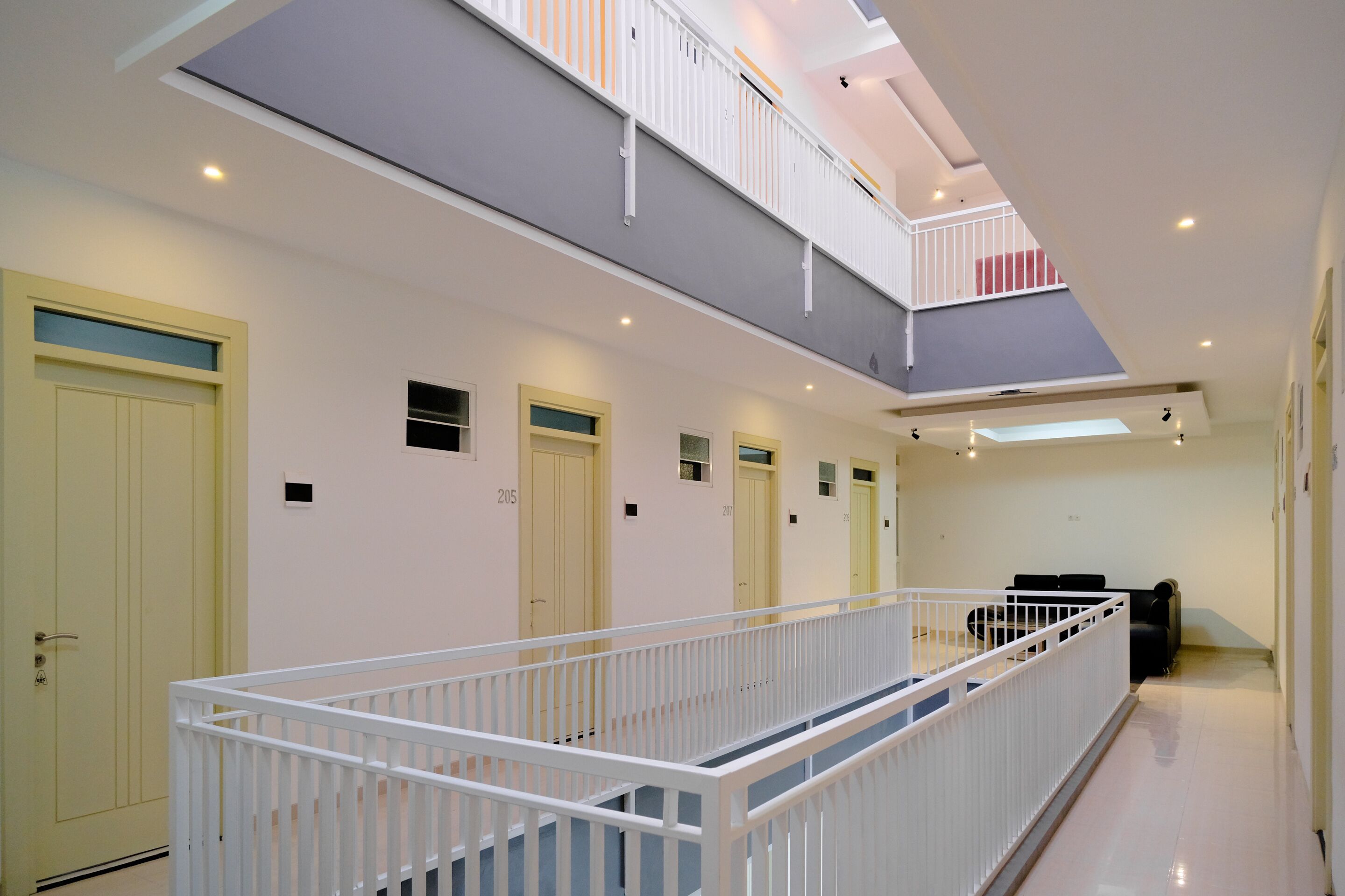 A multi-level hotel corridor with a white railing, doors numbered 205 and 206, and a balcony on the upper level.