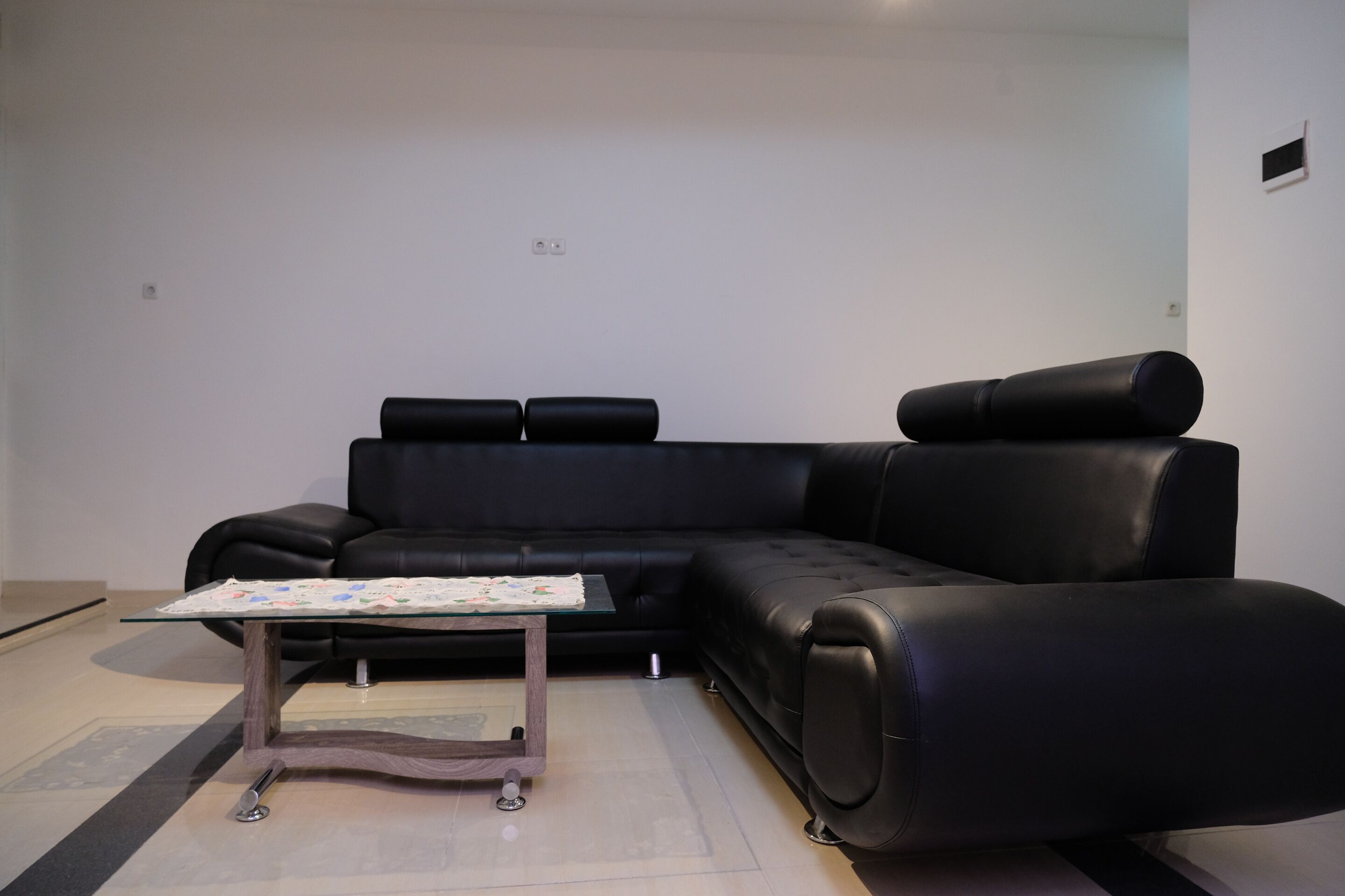Ein modernes Wohnzimmer mit einer schwarzen Ledersofa, einem Glastisch und einem kleinen Beistelltisch.