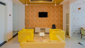 Uma sala de estar moderna com parede de tijolos, TV de tela plana e sofás amarelos.