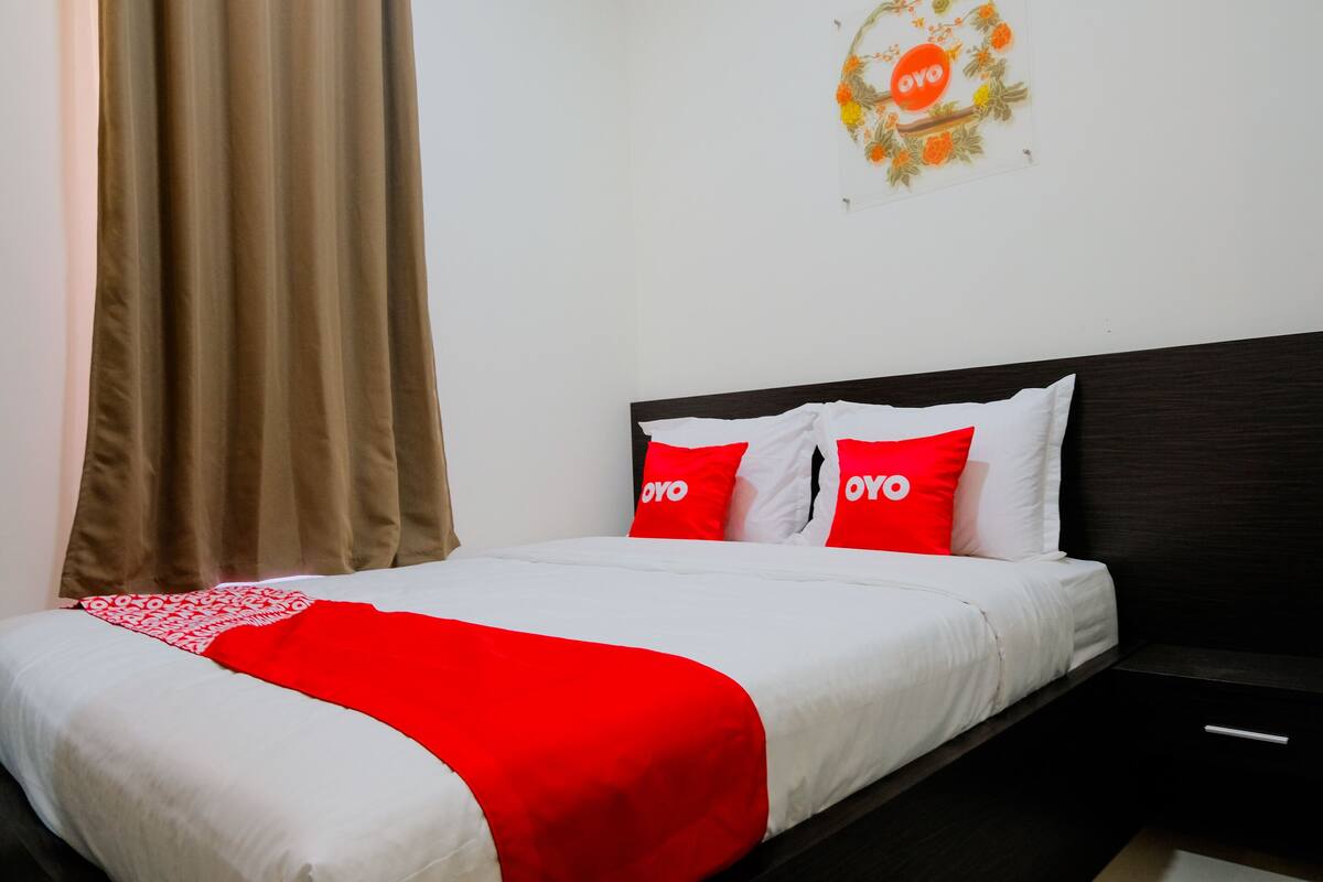 Una cama bien hecha con ropa de cama blanca y roja, un cabecero oscuro y un adorno de pared con la palabra 