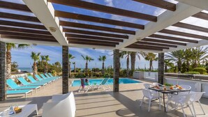 A covered outdoor area with a pool, lounge chairs, and dining tables. - A Truly Spectacular First-Line Sea Front Villa in the beautiful village of Pervolia (Perivolia)
