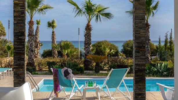 A poolside area with lounge chairs, a small table, and a view of the sea. - A Truly Spectacular First-Line Sea Front Villa in the beautiful village of Pervolia (Perivolia)