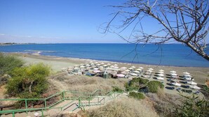 A beach with rows of umbrellas and chairs, a staircase leading down to the beach, and a clear view of the sea. - A Truly Spectacular First-Line Sea Front Villa in the beautiful village of Pervolia (Perivolia)