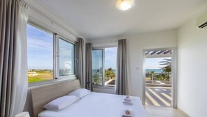 A hotel room with a large bed, a nightstand, and a view of the sea through a sliding door. - A Truly Spectacular First-Line Sea Front Villa in the beautiful village of Pervolia (Perivolia)