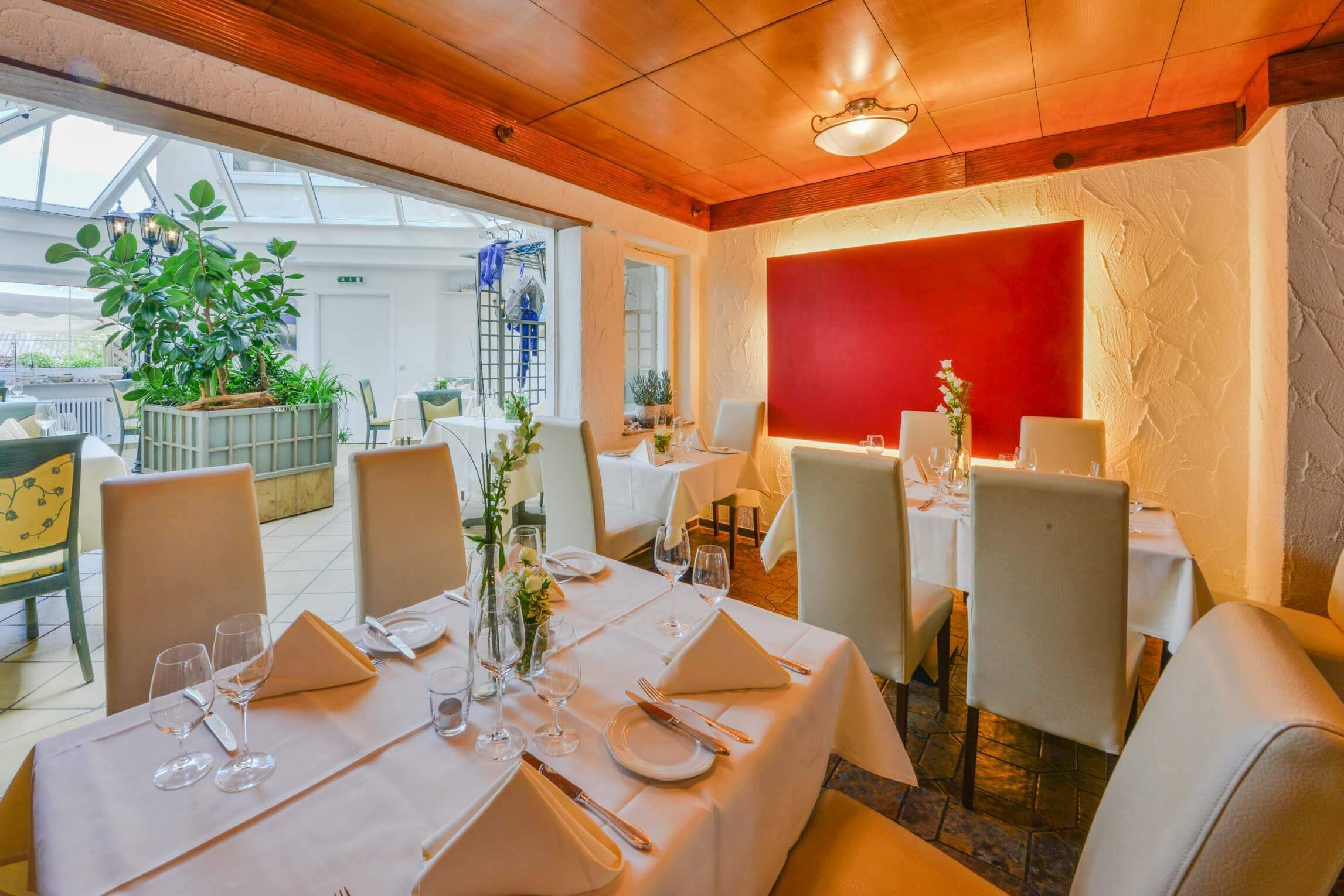 Un espace repas avec des tables dressées pour le service, un grand mur d’accent de couleur rouge et une vue sur la terrasse extérieure.