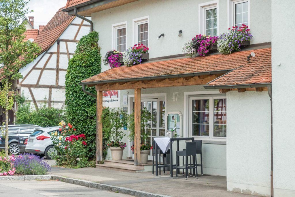 A traditional half-timbered building with a covered outdoor seating area, potted plants, and a sign indicating it is a restaurant.