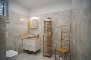 A modern bathroom with a marble wall, a wooden vanity, a white toilet, and a wooden shelf unit. - Villa Marghareta - Deluxe App Marghareta (Dubrovnik)