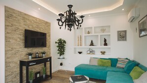 A modern living room with a teal sofa, a black console table, a mounted TV, and a chandelier. - Villa Marghareta - Deluxe App Marghareta (Dubrovnik)