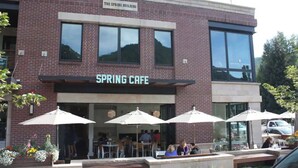 A brick building with a sign reading "SPRING CAFE" and outdoor seating with umbrellas. - Downtown Aspen Studio | Walk to Gondola & Slopes (Aspen)