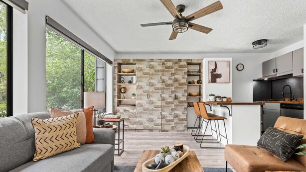 A modern living room with a grey sofa, a wooden coffee table, and a brown leather chair. There is a kitchen area with a wooden countertop and a dining chair. - Downtown Aspen Studio | Walk to Gondola & Slopes (Aspen)