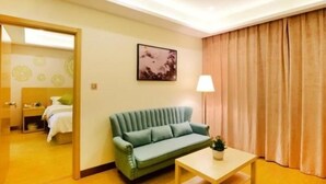 A hotel room with a green sofa, a small table with a plant, a painting on the wall, and a large window with curtains. - GreenTree Inn Ningbo Beilun District Meishan Beach Business Hotel (Ningbo)