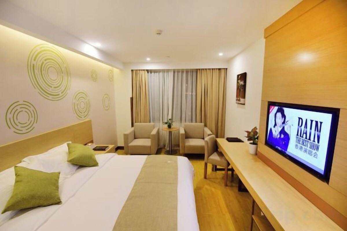 A hotel room with a bed, two chairs, a small table, a TV, and a window with curtains.