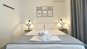 A hotel room with a neatly made bed, two bedside tables with lamps, and a series of framed artworks on the wall. - Feel Athens Studios at Monastiraki (Athens)