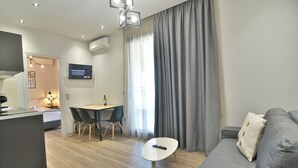 A modern living room with a grey sofa, a small white table, and a dining area with a table and chairs. - Feel Athens Studios at Monastiraki (Athens)