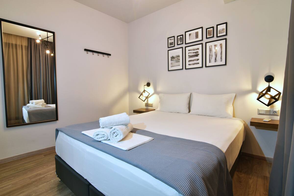 A hotel room with a large bed, a bedside table with a lamp, a mirror, and framed pictures on the wall.