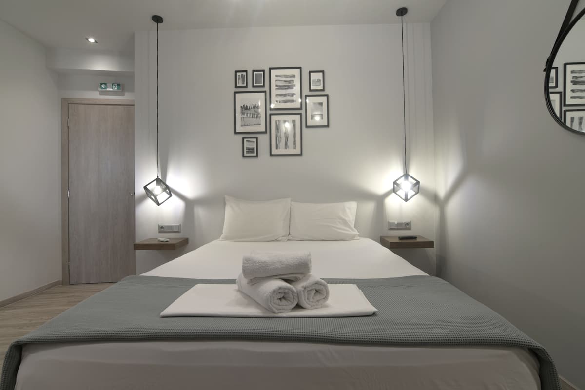 A modern hotel room with a neatly made bed, a wall-mounted artwork arrangement, and a mirror on the wall.