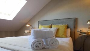 A neatly made bed with rolled white towels, a headboard with a tufted design, and two bedside lamps on nightstands. - Palacete de la Constitución ÁTICO (Málaga)