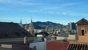 A cityscape with a prominent church spire, residential buildings, and a mountain range in the background. - Palacete de la Constitución ÁTICO (Málaga)