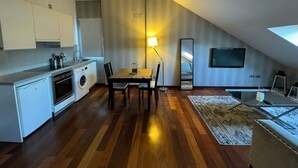 A compact kitchen with modern appliances, a dining area with a table and chairs, and a flat-screen TV mounted on the wall. - Palacete de la Constitución ÁTICO (Málaga)