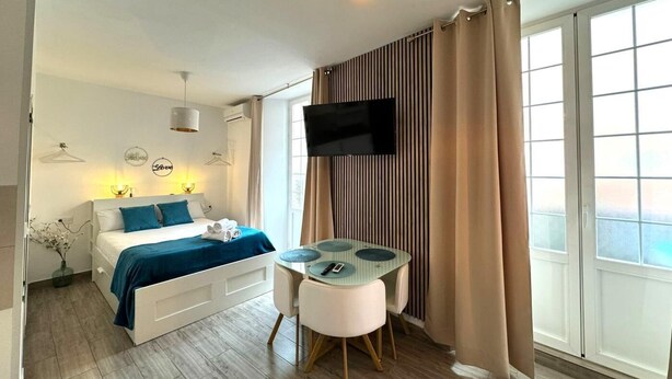 A modern hotel room with a bed, a TV, a small table, and a large window with curtains. - Studio with terrace next to the Atarazanas Market by Málaga Planners (Málaga)