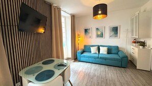 A modern living room with a blue sofa, a glass table with blue placemats, a flat-screen TV mounted on a wooden panel, and a pendant light. - Studio with terrace next to the Atarazanas Market by Málaga Planners (Málaga)