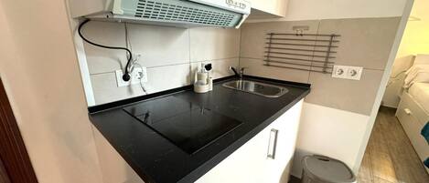 A compact kitchen with a black countertop, white cabinets, a microwave, and a coffee sign on the wall.