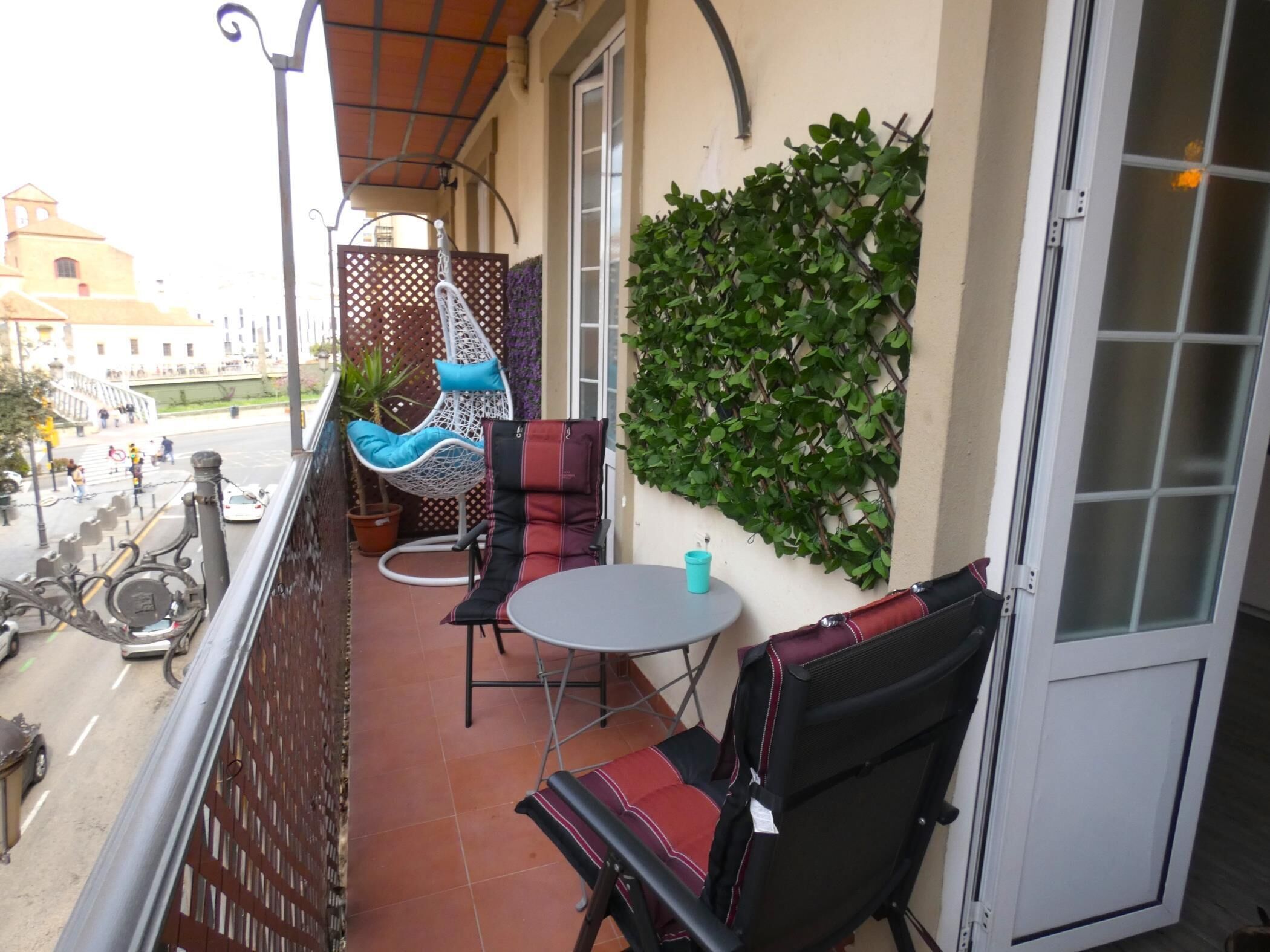 Un balcon avec un espace salon, une plante en pot et une vue sur la rue.