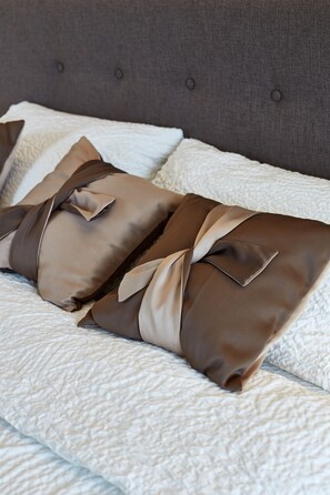 A bed with a grey upholstered headboard and two pillows tied with a beige ribbon. - Riga DeLuxe Apartment (Riga)
