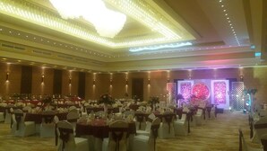 A banquet hall with round tables, white chairs, and a stage with floral decorations. - Hotel Asliya Regency (Mawathagama)