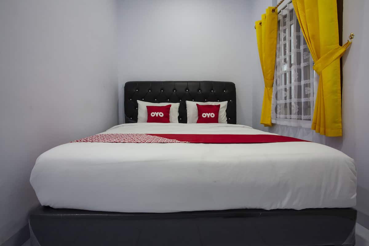 A neatly made bed with white bedding and red pillows, a black headboard, and yellow curtains on a window.